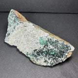 Epidote crystal clusters with dark green and black needle-like formations on a beige and gray rock matrix, displayed against a dark background.