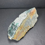Rough gray and brown rock with patches of green epidote crystals clustered along one edge against a dark background