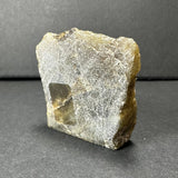 Translucent rough labradorite slab with a rectangular shape showing a pale yellow and gray surface and fibrous texture against a neutral gray background.