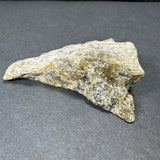 Rough labradorite stone with silvery, golden, and gray iridescent hues resting on a dark gray background, showing a textured, angular surface.