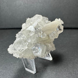 Clear apophyllite crystal cluster with translucent white stilbite on a gray chalcedony base, displayed on a clear acrylic stand against a dark background