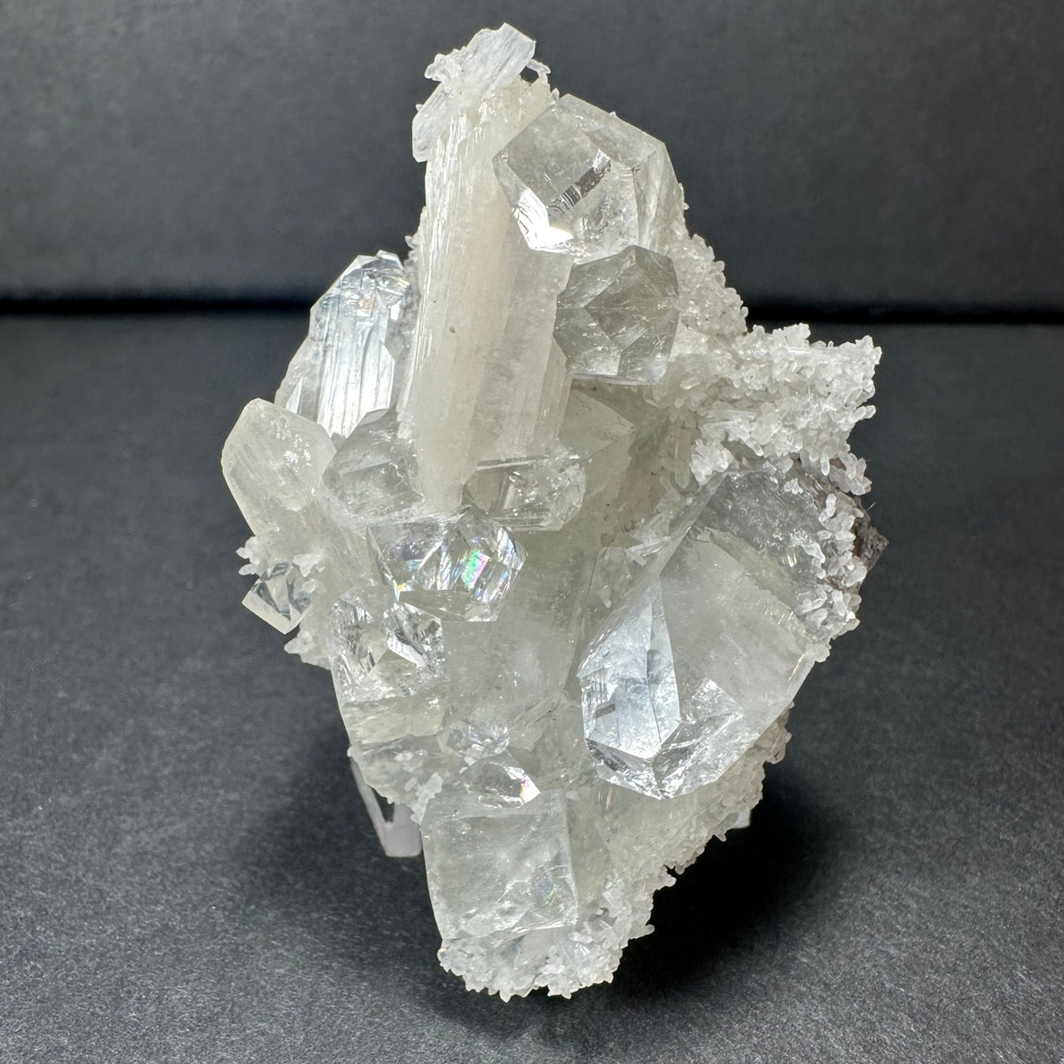 Clear apophyllite crystals with white stilbite clusters on a chalcedony base, displayed against a dark background highlighting their translucent, prismatic forms.