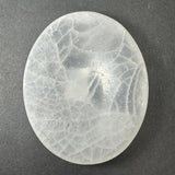 Smooth oval selenite slice with translucent white and cloudy gray patterns against a dark gray background.