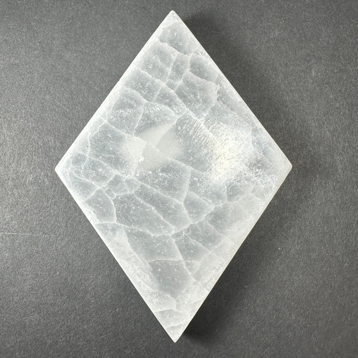 Diamond-shaped small selenite slice with white translucent crystalline texture on dark gray background
