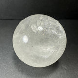 Translucent quartz sphere with cloudy inclusions and subtle internal fractures, resting on a dark textured surface with soft reflections.