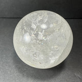 Translucent quartz sphere with internal cracks and inclusions, resting on a dark gray surface against a dark background.