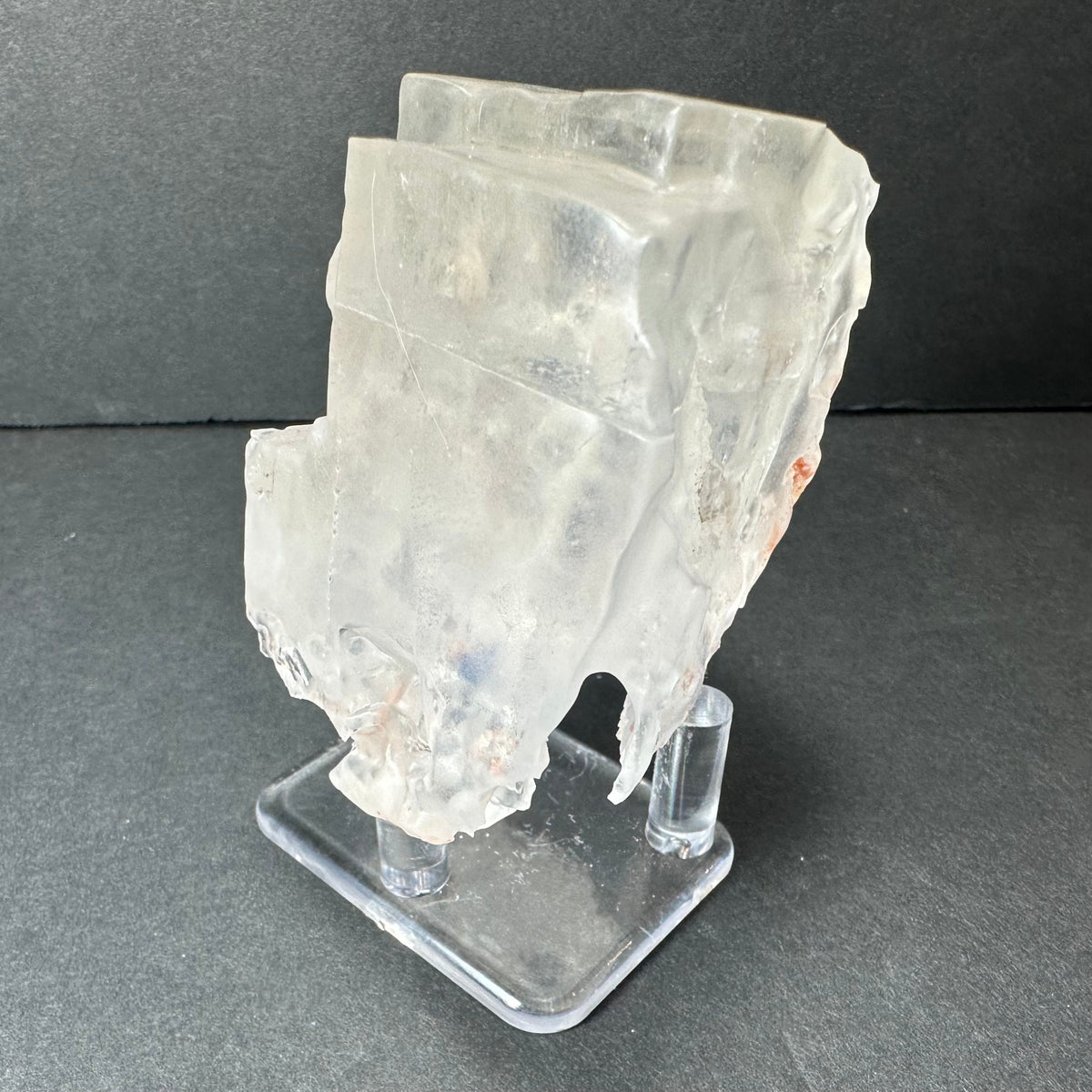 Colorless cubic fluorite crystal from Hardin County, Illinois, shown translucent with irregular edges on a clear acrylic stand against a dark background