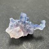 Translucent blue fluorite cube with irregular edges and a frosted crystalline surface, resting on a dark textured background.