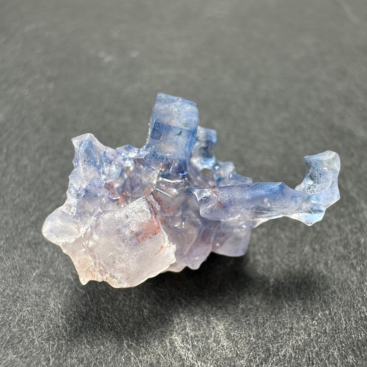 Translucent blue fluorite cube with irregular edges and a frosted crystalline surface, resting on a dark textured background.