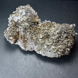Chunky cluster of metallic golden marcasite crystals densely covering translucent white calcite with scattered angular quartz prisms on a dark background
