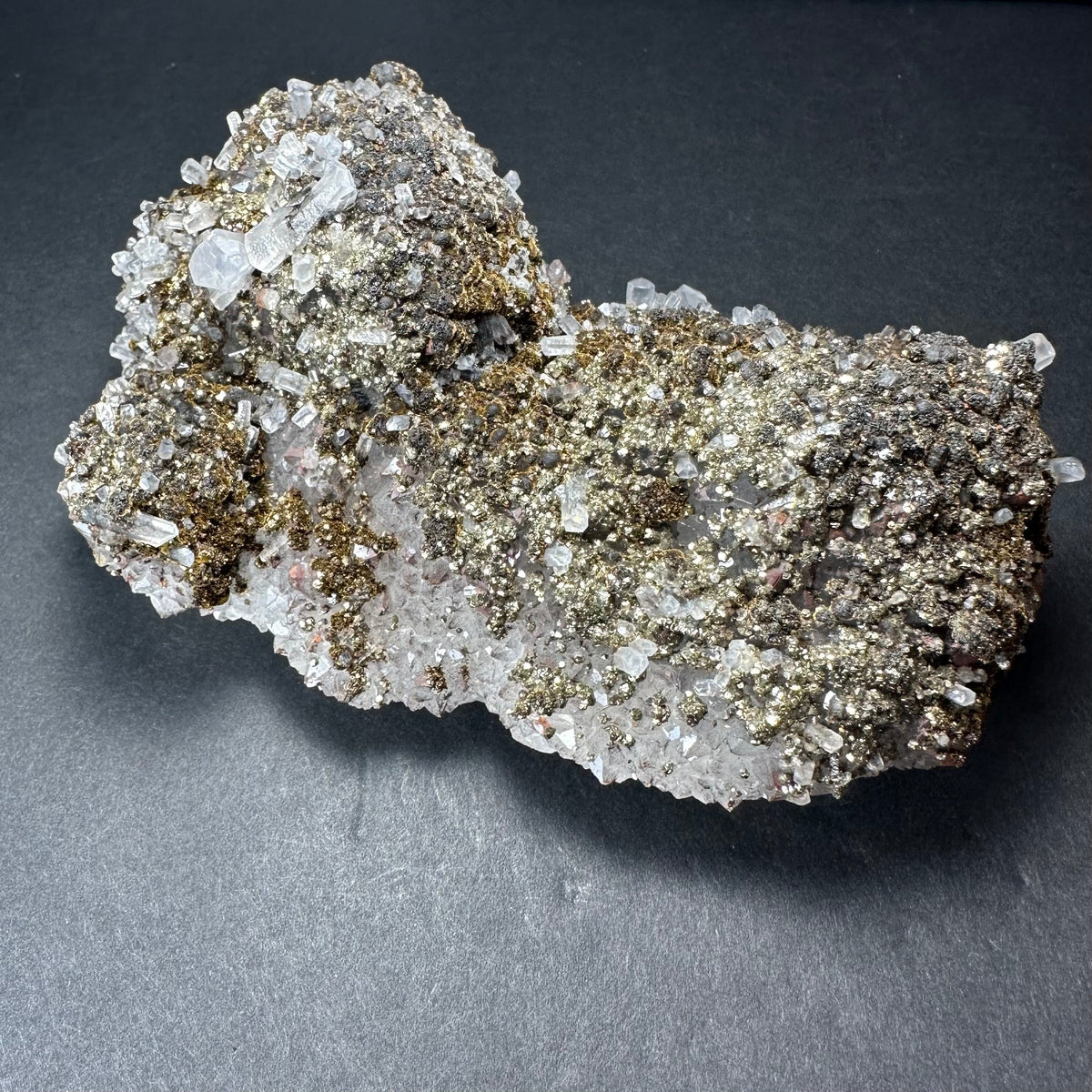 Chunky cluster of metallic golden marcasite crystals densely covering translucent white calcite with scattered angular quartz prisms on a dark background