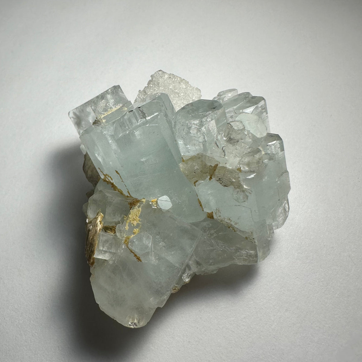 Cluster of translucent aquamarine crystals with pale blue hues and natural golden-brown inclusions, shown on a white background from above.
