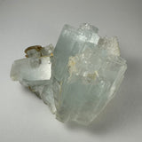 Translucent pale blue aquamarine crystal cluster with prismatic hexagonal formations, set against a plain light gray background, highlighting natural clarity and structure.