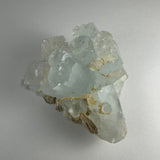 Light blue aquamarine crystal cluster with transparent cubic formations and beige matrix base on a neutral background.