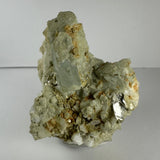 Rough aquamarine crystal embedded in a beige feldspar, albite, and mica matrix with earthy brown patches, displayed against a neutral background.