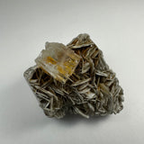 Transparent aquamarine crystal with yellow inclusions atop layered, silvery muscovite mineral cluster on a white background