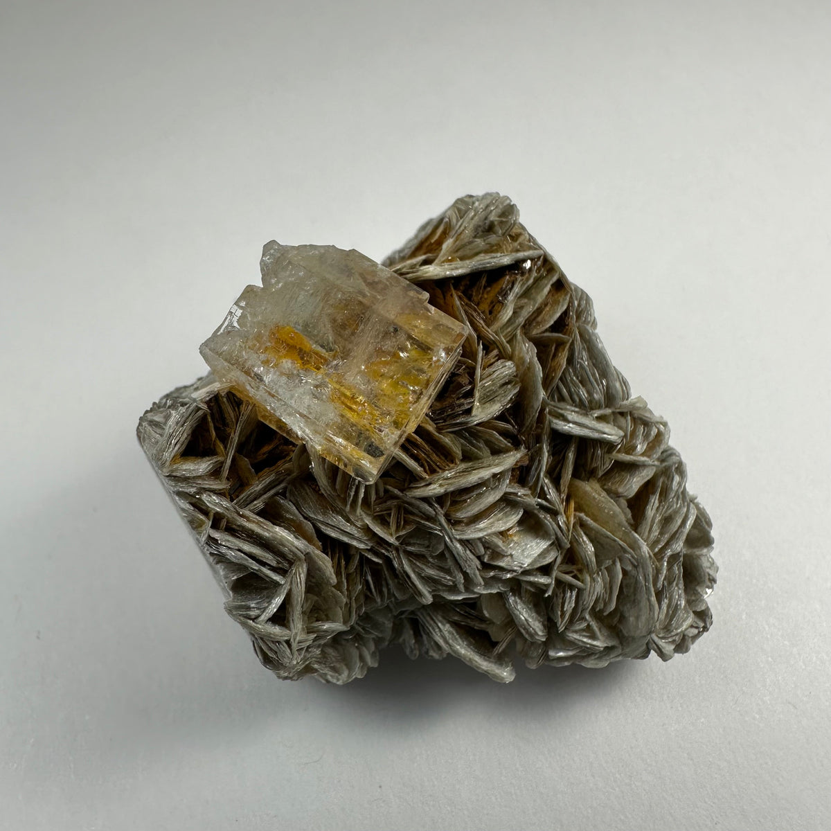 Transparent aquamarine crystal with yellow inclusions atop layered, silvery muscovite mineral cluster on a white background