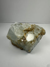 Chunk of aquamarine with translucent pale blue crystals and tan muscovite flakes clustered on top, displayed against a plain white background.
