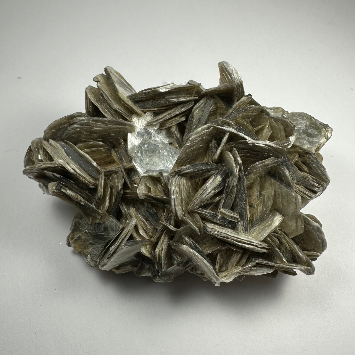 Cluster of shiny, silver-gray muscovite crystals surrounding a translucent, aquamarine gemstone on a neutral background, highlighting layered, flaky textures and a faceted central gem.
