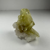 Translucent yellow-green brazilianite crystal cluster on white albite crystals, shown against a neutral light background.