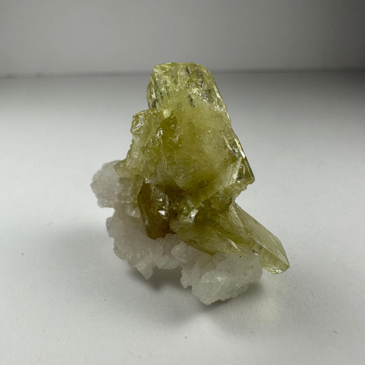 Translucent yellow-green brazilianite crystal cluster on white albite crystals, shown against a neutral light background.