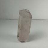 Translucent pale pink terminated spodumene kunzite crystal with a blocky shape standing upright on a white surface against a neutral background.