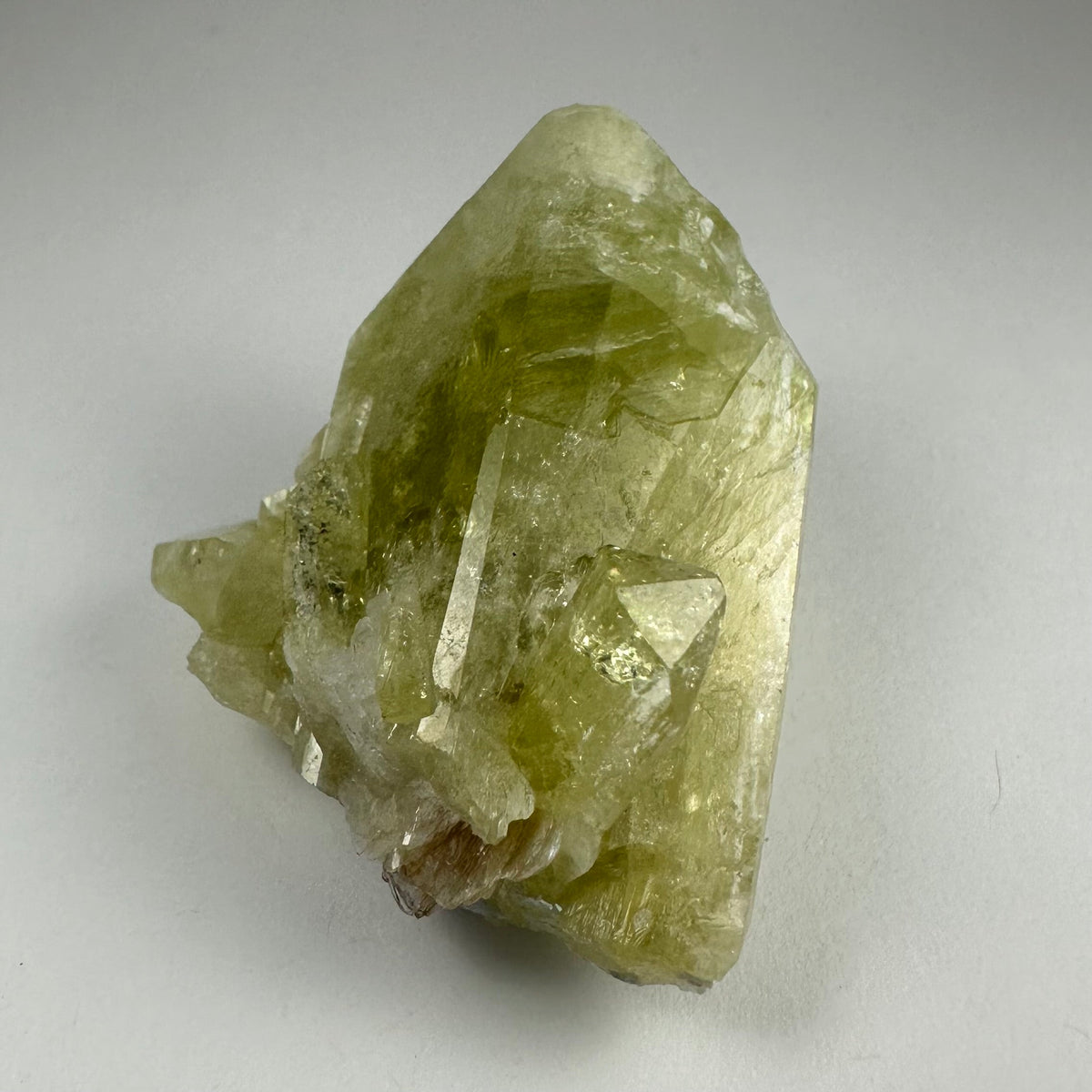 Translucent pale yellow-green Brazilianite crystal with sharp edges and natural surface irregularities on a neutral background