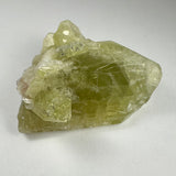 Translucent yellowish-green Brazilianite crystal with angular facets and rough texture, resting on a plain white background.