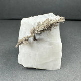Chunk of white calcite with a jagged, silvery native silver dendritic formation extending across the top and side edges against a gray-black background.