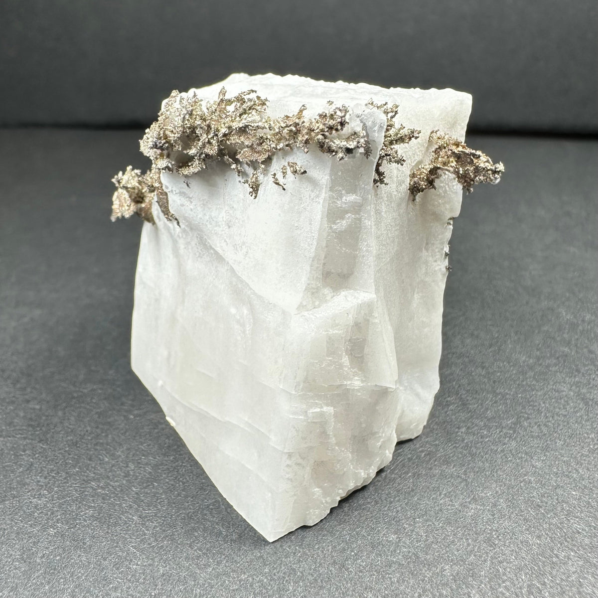 White translucent calcite crystal with dendritic native silver formations along the top edge, displayed on a dark gray surface.