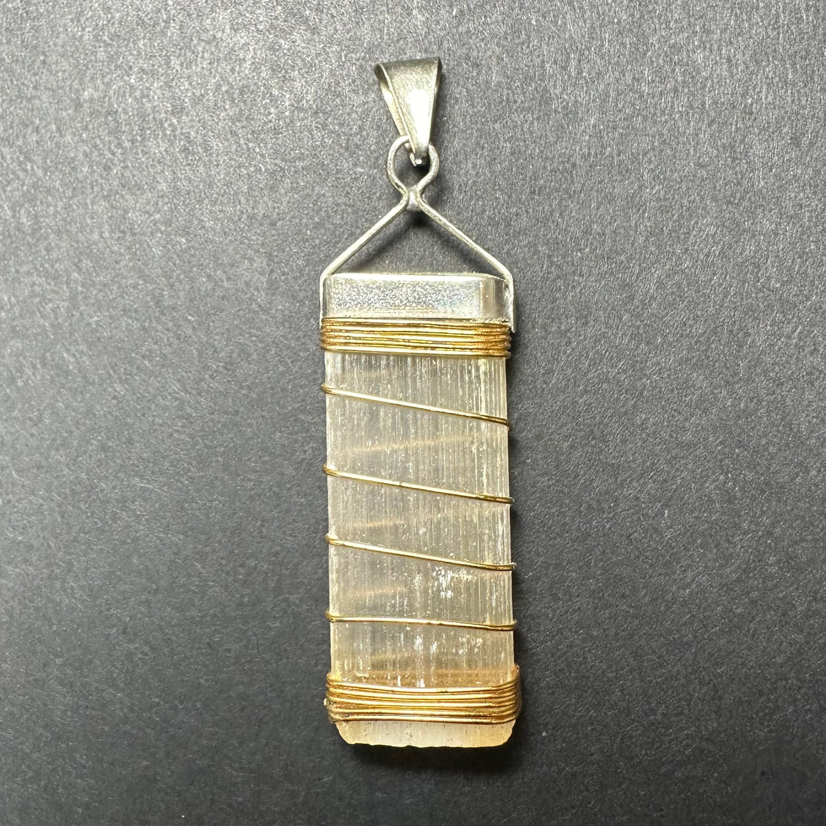 Rectangular translucent selenite pendant wrapped with thin gold wire and topped with a textured sterling silver triangular clasp on a dark gray background