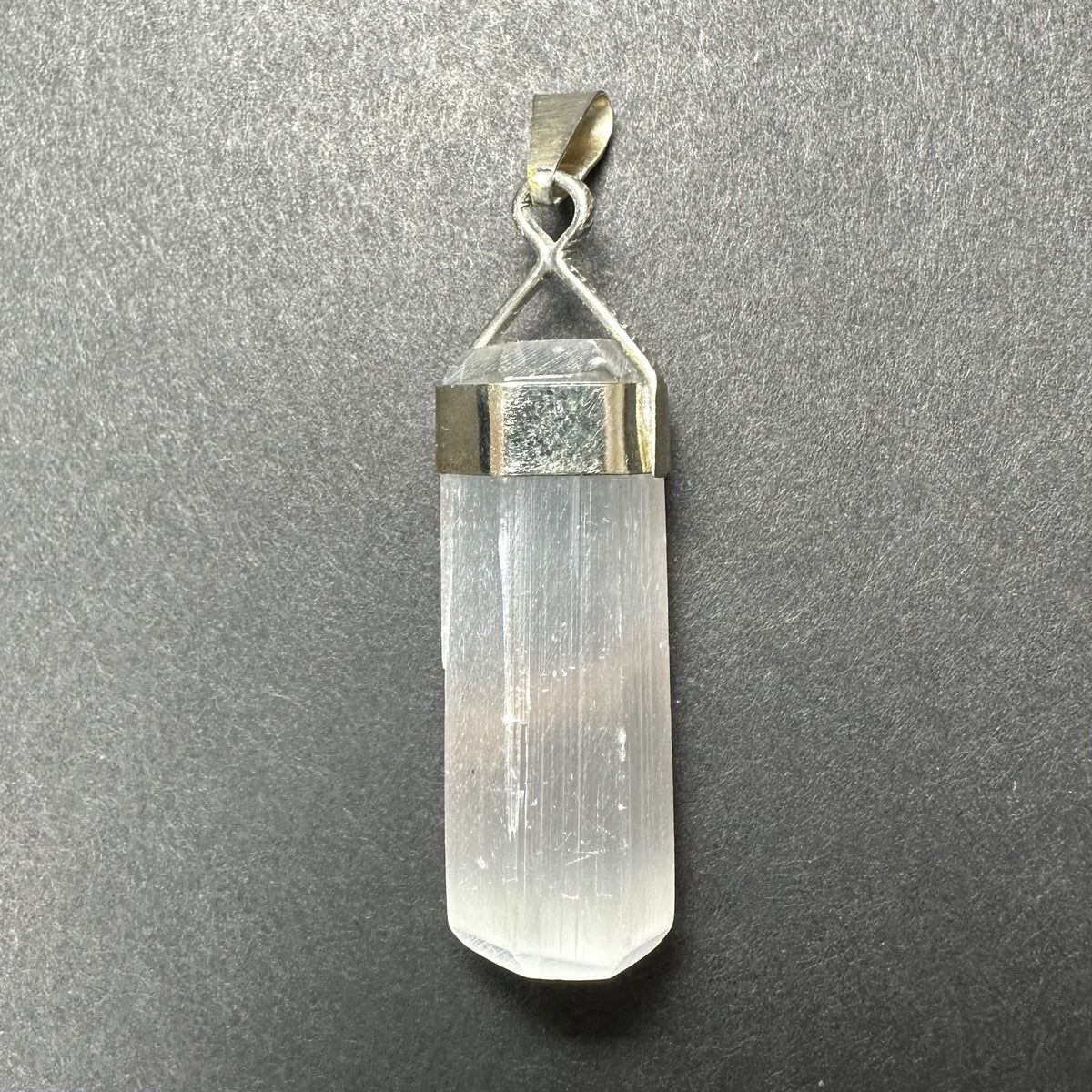 Clear selenite crystal pendant with smooth, translucent surfaces set in a polished sterling silver clasp against a textured gray background.