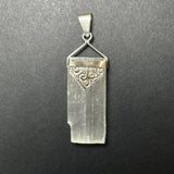 Rectangular translucent selenite pendant with vertical striations, topped with a decorative sterling silver clasp featuring a floral swirl pattern and triangular detail.