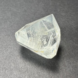 Transparent white topaz crystal with clear facets and subtle internal textures, resting on a textured gray surface.
