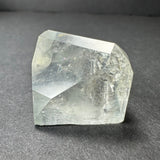 Clear and slightly cloudy white topaz crystal with natural faceted surfaces resting on a dark gray background, showing internal textures and light reflections.