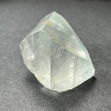 Translucent white topaz crystal with natural faceted surfaces and subtle internal inclusions, resting on a dark gray textured surface.