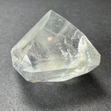 Translucent white topaz crystal with sharp, faceted edges and natural inclusions, resting on a dark gray textured surface.