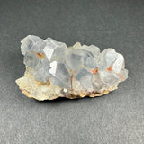 Cluster of translucent pale blue celestite crystals with hexagonal shapes on a light brown matrix, displayed against a dark gray textured background.