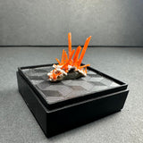 Cluster of vibrant orange crocoite crystals growing upright from a white matrix, displayed on a textured black platform with a geometric pattern.