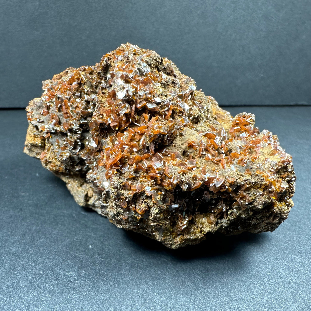 Cluster of bright orange wulfenite crystals on rough beige and brown matrix from Maoniuping Mine, Sichuan, China, shown with detailed crystal facets and natural texture.