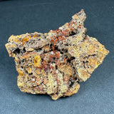 Wulfenite crystal cluster with translucent brown-orange cubic crystals on a rough, textured matrix with yellowish patches against a dark background.