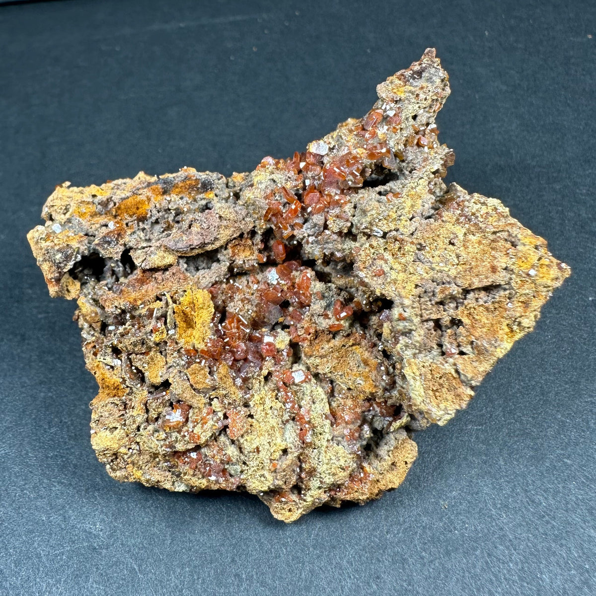 Wulfenite crystal cluster with translucent brown-orange cubic crystals on a rough, textured matrix with yellowish patches against a dark background.