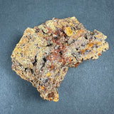 Brown and orange wulfenite crystal cluster embedded in rough matrix rock with granular texture against a dark background.