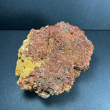 Cluster of reddish-brown vanadinite crystals densely covering a yellowish-brown matrix, displayed on a dark background.