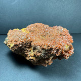 Cluster of small, shiny orange-red vanadinite crystals densely covering a rough, dark brown rock matrix against a dark gray background