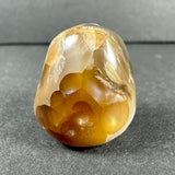 Polished Fire Agate stone displaying translucent golden-brown hues with iridescent flashes and natural crystalline patterns against a gray background.
