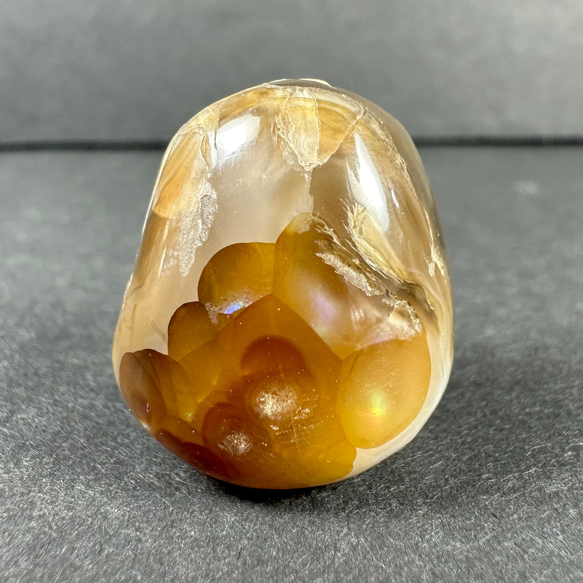Polished Fire Agate stone displaying translucent golden-brown hues with iridescent flashes and natural crystalline patterns against a gray background.