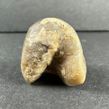 Beige and light brown irregularly shaped stone with a rough texture, positioned upright against a gray surface and background.