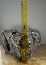 Three ammonite fossils embedded in textured brown matrix stones with a yellow ruler standing vertically in front for scale, showing around 6 inches tall.