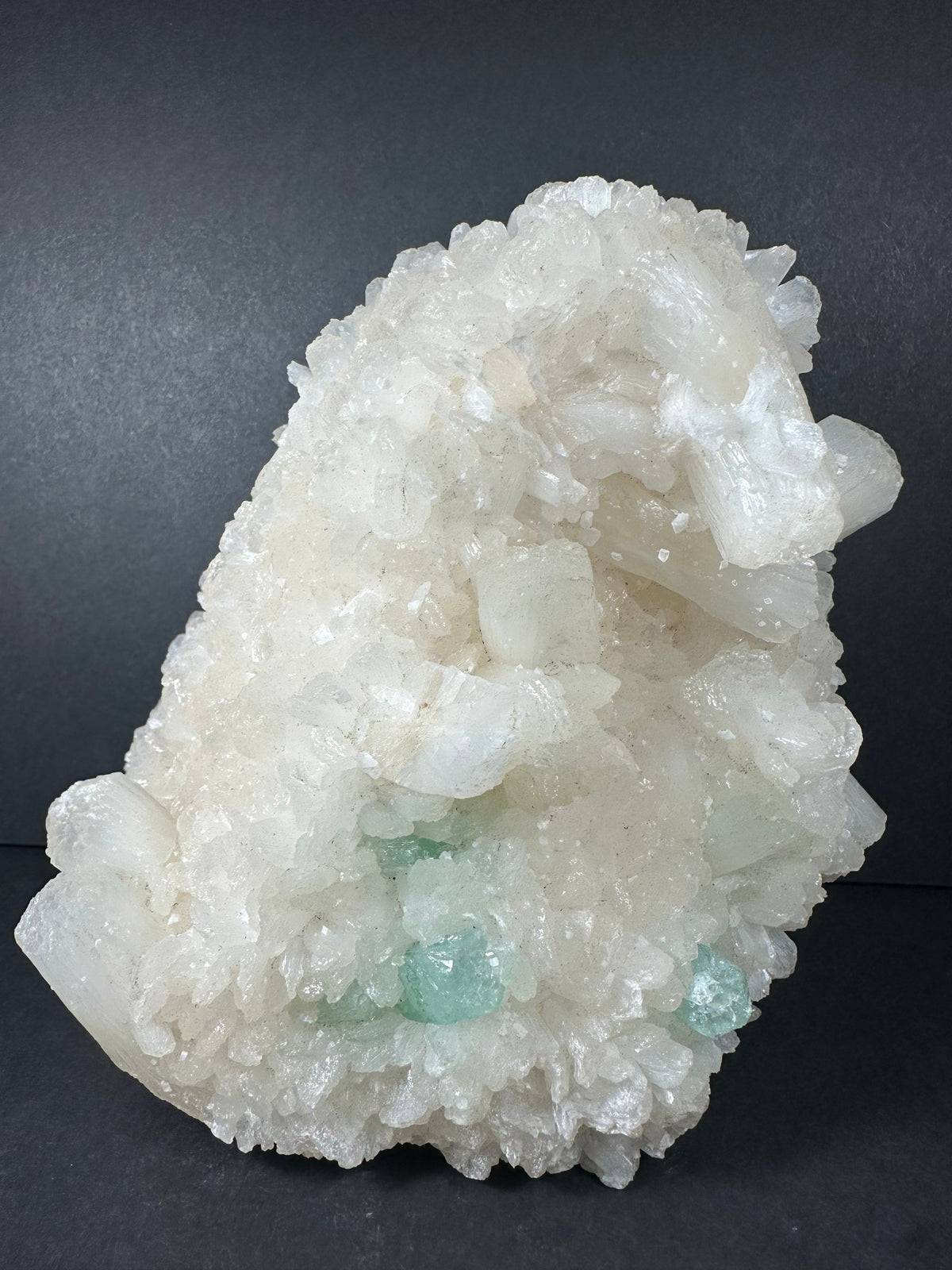 Cluster of translucent white stilbite crystals with small patches of light green apophyllite, arranged on a dark background showing crystalline texture and layering.